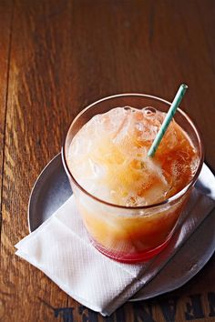 a glass filled with ice sitting on top of a wooden table next to a napkin