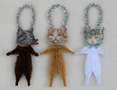 three cats are hanging from the handles of christmas decorations, one is wearing a cat's head