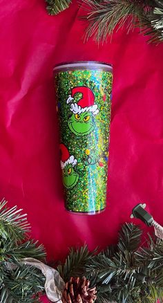 a christmas cup with the grin on it sitting next to pine cones and evergreen branches