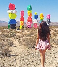 a girl walking in the desert with large sculptures behind her