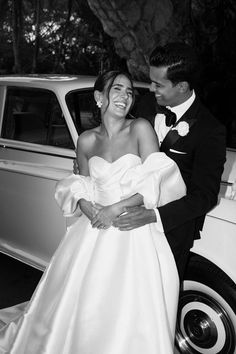 a bride and groom standing in front of a car