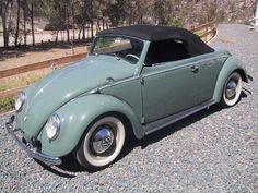 an old green car is parked on the gravel