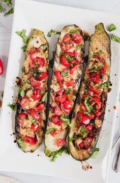 grilled eggplant with tomatoes and herbs on a white plate next to silverware