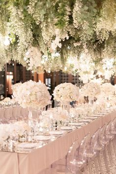 the tables are set with clear chairs and white flowers hanging from the ceiling above them