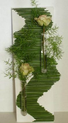 three vases with flowers and greenery in them sitting on a table next to a wall