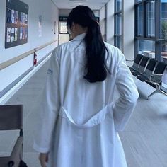 a woman in a white lab coat is walking down the hall with her back to the camera