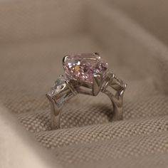 a pink diamond ring sitting on top of a white cloth