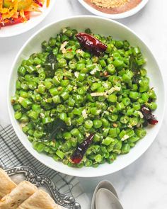 a white bowl filled with green peas next to two bowls of salad and pita bread