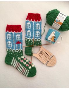 two knitted socks with houses on them next to a ball of yarn and knitting needles