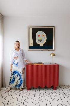 a woman standing next to a red cabinet in front of a painting on the wall