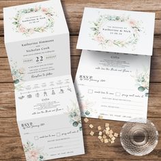 the wedding stationery is laid out on top of a wooden table next to a glass of wine