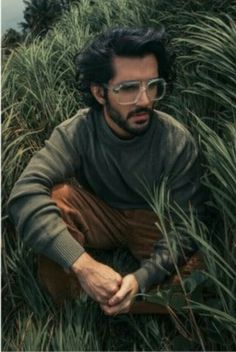 a man sitting in tall grass wearing glasses