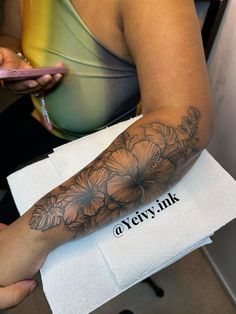 a woman with a flower tattoo on her arm holding a cell phone in her hand