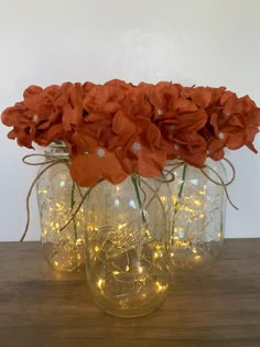 three mason jars filled with red flowers and fairy lights