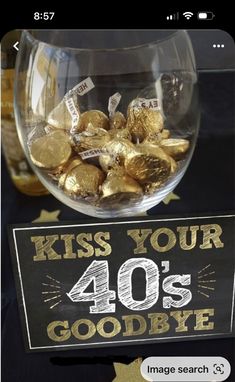 a glass bowl filled with gold foiled candies next to a sign that says kiss your 40's goodbye