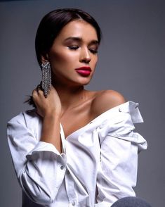 a woman wearing a white shirt and holding a pair of earrings