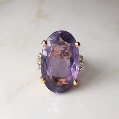 A Vintage 14 carat Gold Amethyst ring framed by diamonds. This beautiful piece displays a gorgeous purple stone in the clutches of a striking gold setting. The shoulders offer a really simple design, but why would it offer anything else, the setting holds so much sparkle and with the stone it's an absolute show stopper! CONDITION: Wear consistent with age and use. Please see photos for more detail. AMETHYST DIAMETER: 25mm x 15mm BAND WIDTH (NARROWEST): 2mm DIAMOND DIAMETER: 1.5mm RING SIZE: UK: P 1/2 | US: 7 3/4 WEIGHT: 12.4 grams (QZZ)