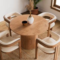 a round wooden table with four chairs around it and a vase on the table top