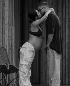 a black and white photo of a man kissing a pregnant woman