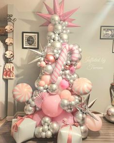 a pink and silver christmas tree decorated with balloons, starbursts, candy canes and other decorations