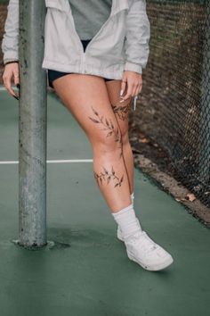 a woman with tattoos standing next to a pole on a tennis court holding a racket