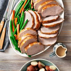 sliced pork, green beans and carrots on a white plate next to a bowl of potatoes