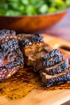 some meat is sitting on a cutting board next to a bowl of greens and a fork