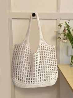 a white crocheted bag hanging on the wall next to a vase with flowers