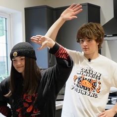 two young people standing next to each other in a kitchen