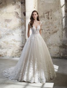 a woman in a white wedding dress standing next to an old brick wall with sunlight streaming through the window