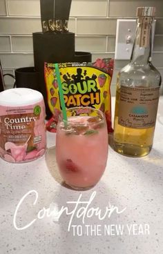 a pink drink sitting on top of a counter next to two bottles of liquid and a bag