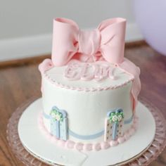 a white cake with pink bows on top sitting on a glass platter next to a balloon