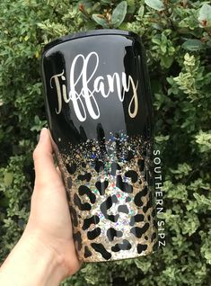 a hand holding up a black wine glass with gold glitter and leopard print on it