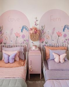 two twin beds with pink and purple comforters in a girls'bedroom, the wall has flowers painted on it