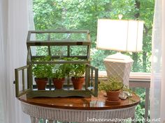 a table with some plants on it and a lamp in the window sill next to it