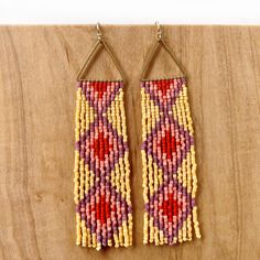 two pairs of beaded earrings hanging from hooks on a wooden surface with wood planks