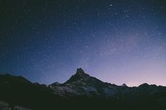 the night sky is lit up with stars above a snowy mountain range and snow - capped mountains