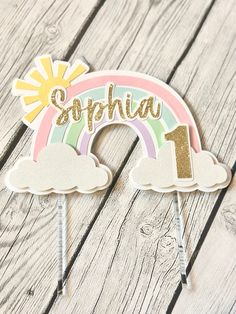 a cake topper with the number one on it and a rainbow in the background