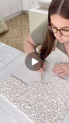 a woman in glasses is making something out of white paper with scissors and thread on the table