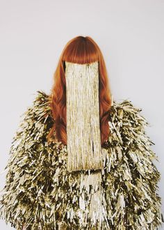 a woman with long red hair wearing a gold and silver feathered cape over her head