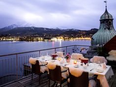 an outdoor dining area overlooking the water at night with lights on and snow covered mountains in the background