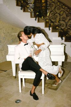 two people sitting on a white chair kissing each other in front of a stair case