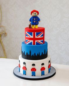 a three tiered cake decorated with the british flag and teddy bear on it's top