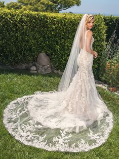 a woman in a wedding dress is standing on the grass with her veil over her head