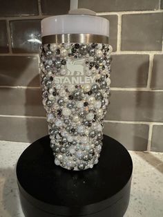 a coffee cup with beads on it sitting on top of a black stand in front of a brick wall