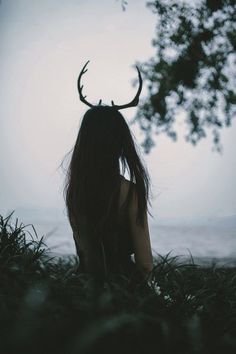 a woman sitting in the grass with a deer's antlers on her head