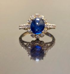 "DeKara Designs Collection Art Deco Inspired Extremely Elegant Halo Opal Diamond Engagement Ring. Metal- 90% Platinum, 10% Iridium. Stones- 1 Natural Oval Cabochon Ceylon Blue Sapphire 2.85 Carats, 26 Round Diamonds F-G Color VS1 Clarity 0.65 Carats. Size- 4-12 An Amazing Art Deco Inspired Ceylon Blue Sapphire Halo Diamond Engagement Ring Made in 18K Yellow Gold. The ring features a beautiful a beautiful Ceylon Blue Sapphire that is Oval in shape and cabochon cut. The sapphire is gracefully set Luxury Hallmarked Oval Cabochon Sapphire Ring, Formal Yellow Gold Cabochon Sapphire Ring, Luxury Sapphire Cabochon Ring For Anniversary, Yellow Gold Sapphire Diamond Ring With Oval Cabochon, Yellow Gold Sapphire Ring With Diamond Oval Cabochon, Timeless Blue Oval Cabochon Jewelry, Oval Cabochon Sapphire Ring In Yellow Gold With Diamond, Luxury Yellow Gold Halo Ring With Gemstone, Luxury Cabochon Sapphire Ring For Wedding