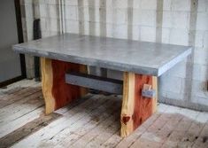 a table made out of wood and concrete on top of a wooden floor in front of a brick wall