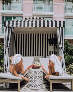 two women in bathing suits sitting on chaise lounges next to a hotel pool