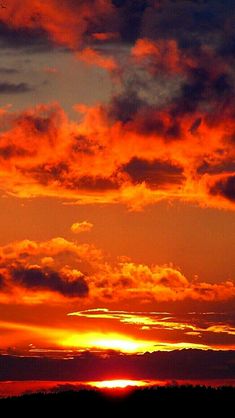 an airplane flying in the sky at sunset with clouds and trees around it, as the sun is setting